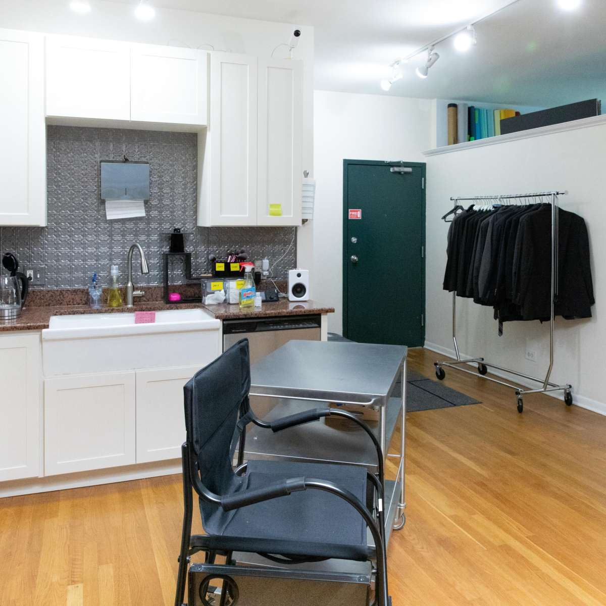 A modern kitchen space with a dining table and chairs, a clothing rack with jackets, and two doors leading to other rooms.