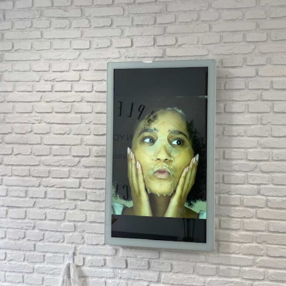 A framed portrait of a woman with an expressive face and wet hair mounted on a brick wall.