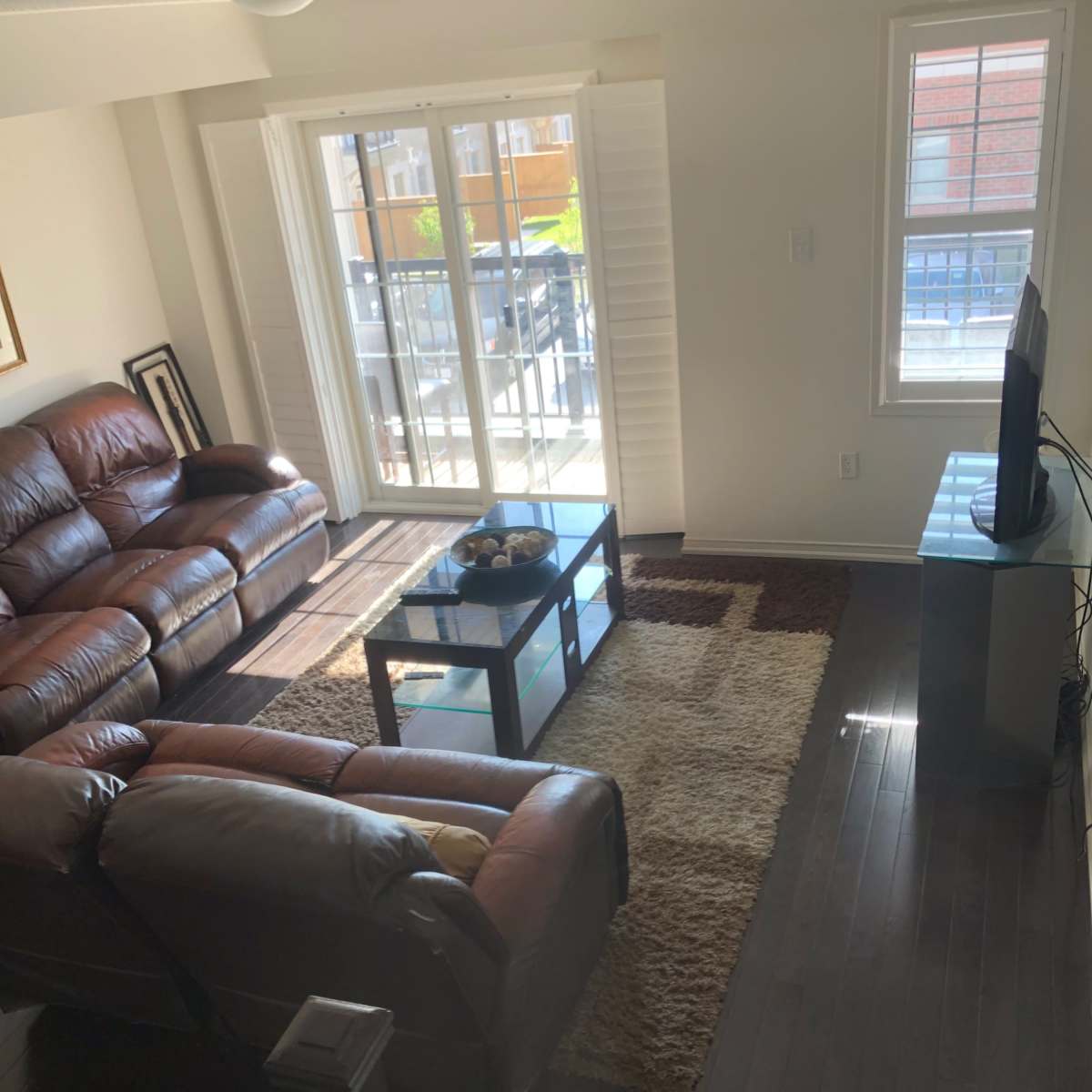 A living room with two dark leather sofas, a coffee table on a rug, and a television against a wall with windows letting in natural light.