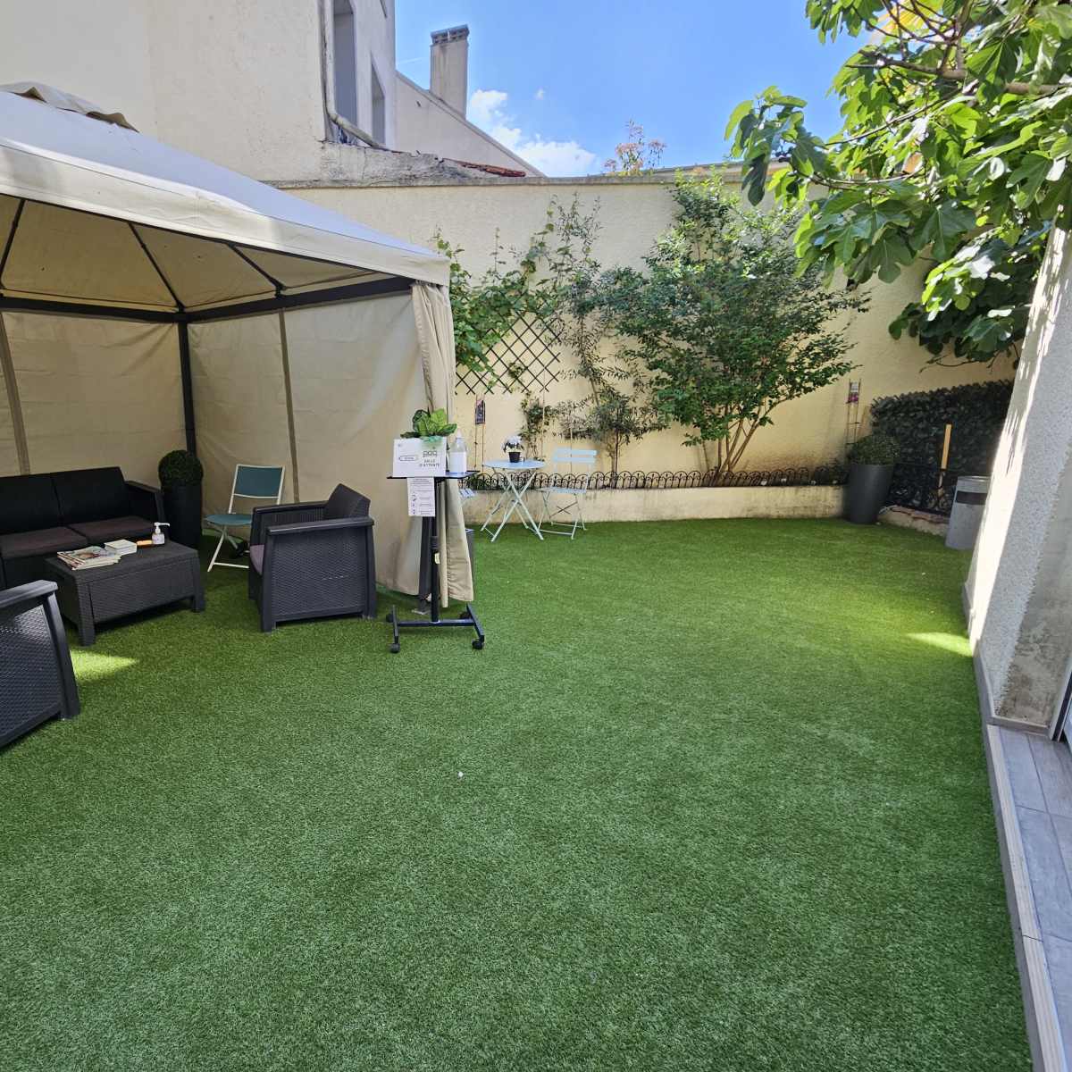 A small outdoor area featuring a tent with seating, artificial grass, and potted plants.