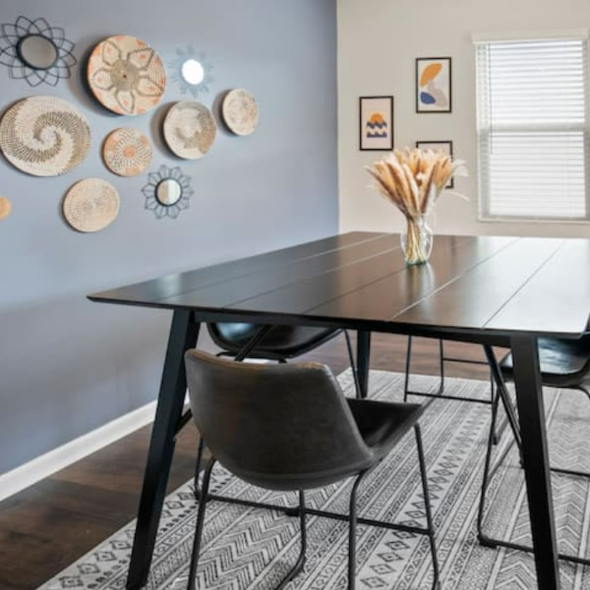 A dining area features a black table with three chairs, surrounded by patterned wall decor and a light-colored rug.