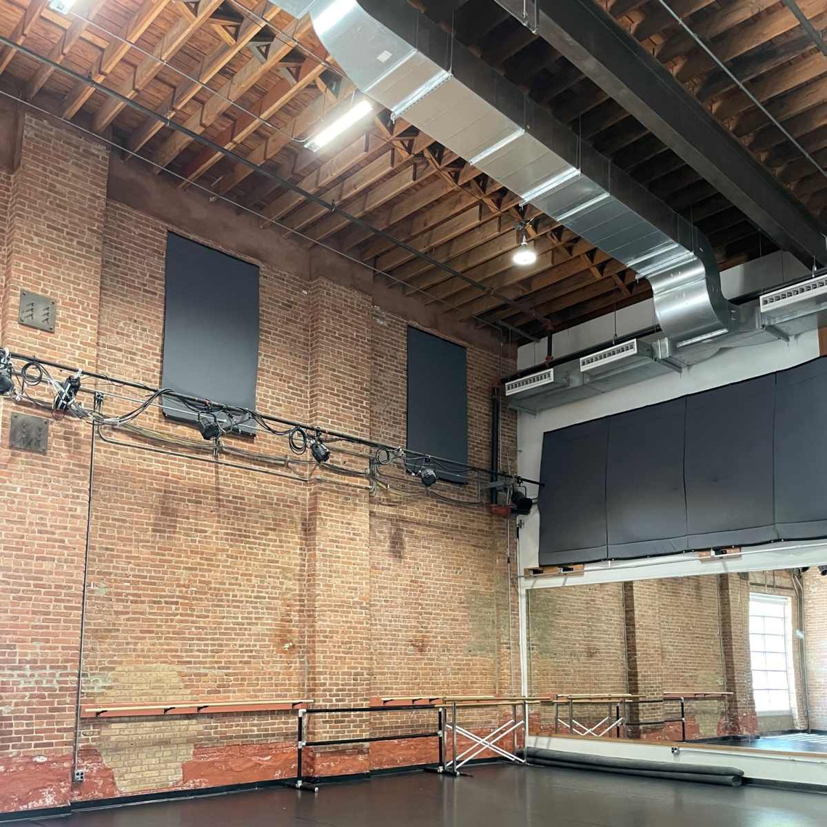 A spacious dance studio with exposed brick walls, a mirrored wall, and a dark wooden floor.