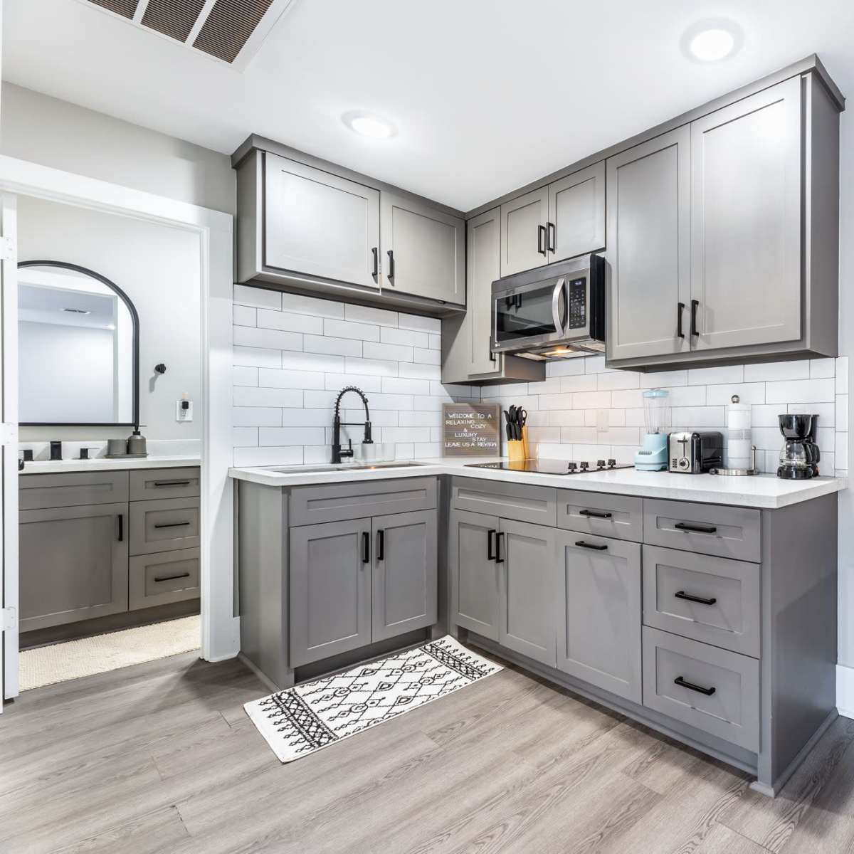 A modern kitchen featuring gray cabinets, a countertop with a sink and stove, a microwave, and a small refrigerator.