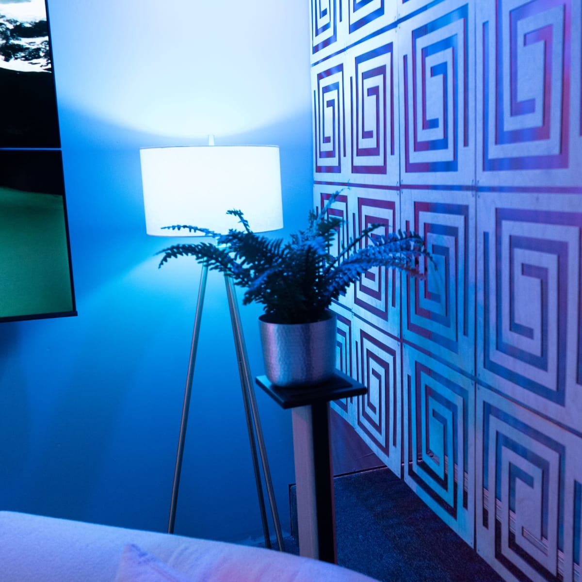 A corner of a room featuring a patterned wall, a floor lamp, and a potted plant on a stand.
