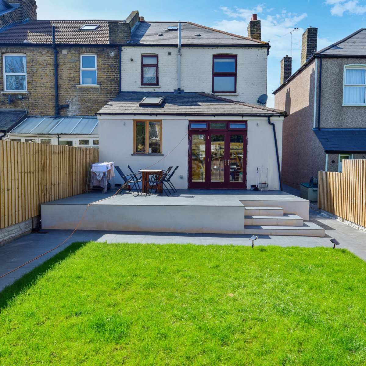 A backyard with a lawn, a paved patio area, and a two-story house in the background, enclosed by wooden fences.