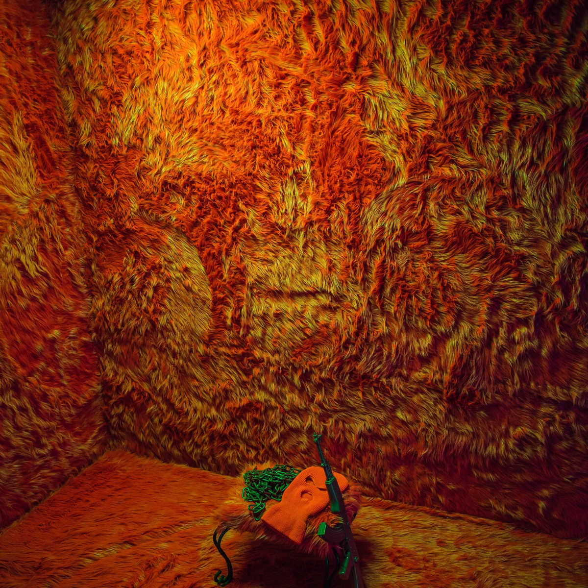 A plush orange-hued room with fuzzy walls contains a small table holding a green object and a rifle.