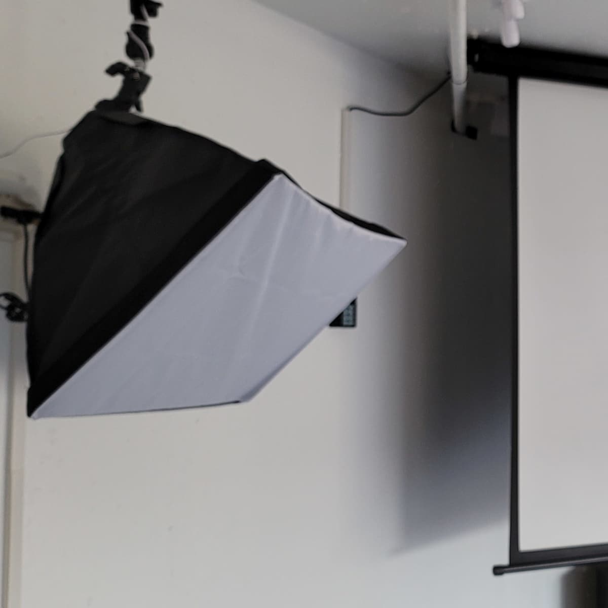 A black and white softbox is mounted on the wall next to a retractable white projection screen.