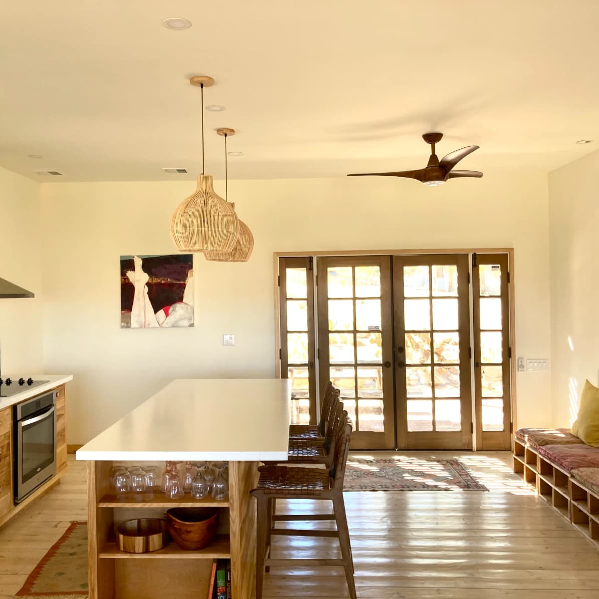 A modern kitchen with a large island, wooden cabinetry, and a set of double doors leading to an outdoor area.