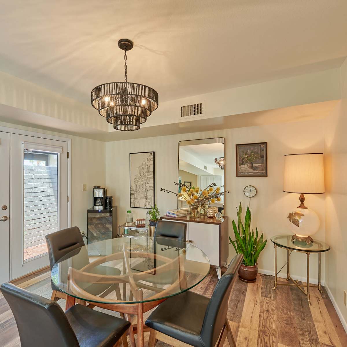 A dining area featuring a glass table with black chairs, a decorative chandelier, and sliding glass doors leading to an outdoor space.