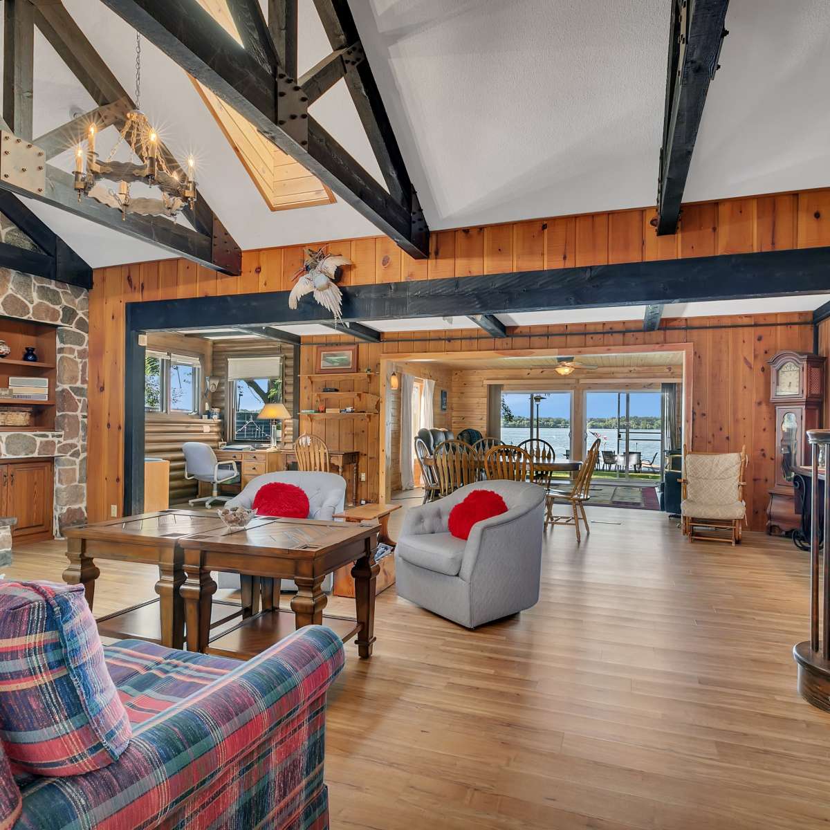 A spacious living area featuring wooden beams, a stone fireplace, and large windows that provide a view of the outside.