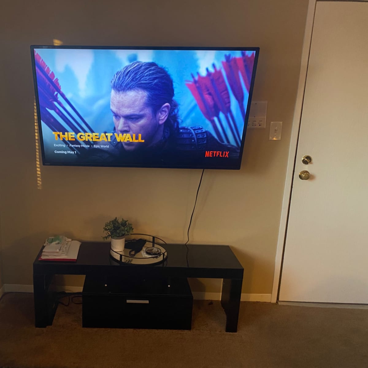A flat-screen TV mounted on a wall displays the title "The Great Wall" alongside promotional content from Netflix, with a black TV stand underneath.