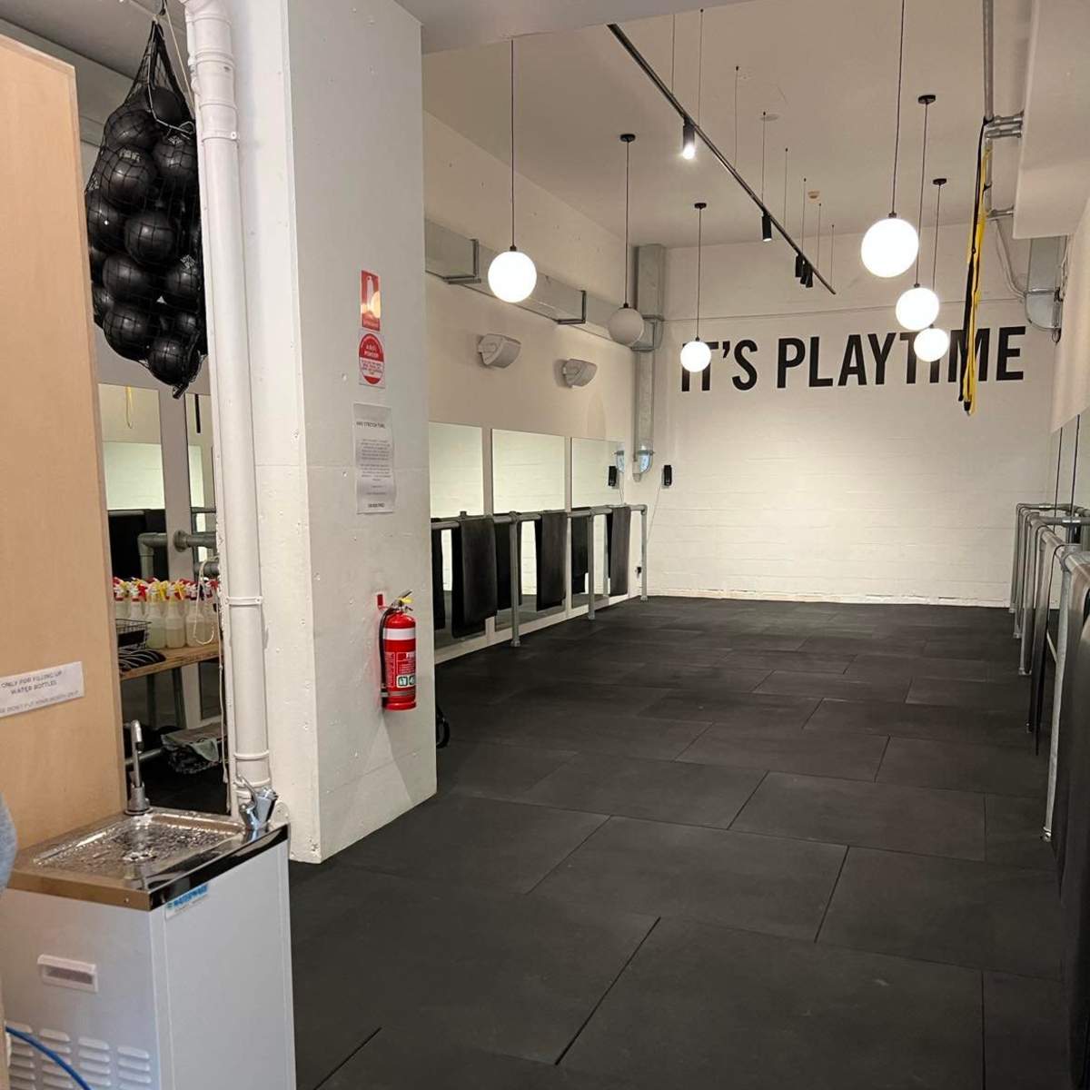A spacious indoor area with black rubber flooring, ceiling lights, and a wall featuring the text "IT'S PLAYTIME."