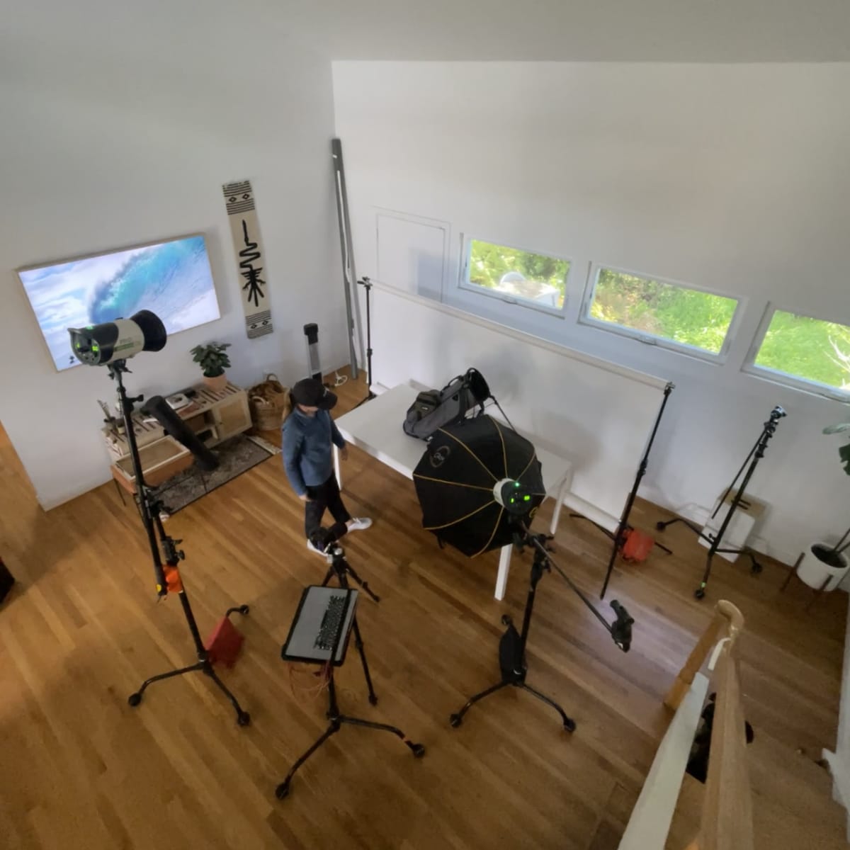 A person stands in a well-lit room filled with photography equipment, including tripods, a backdrop, and studio lights.