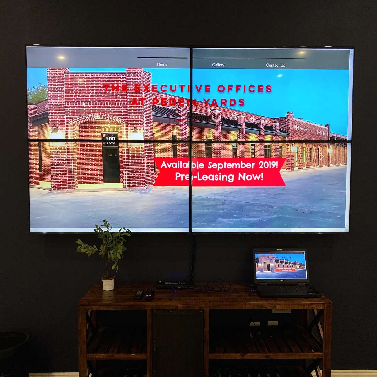 A large screen displays information about available executive office space for lease, alongside a laptop on a wooden table.
