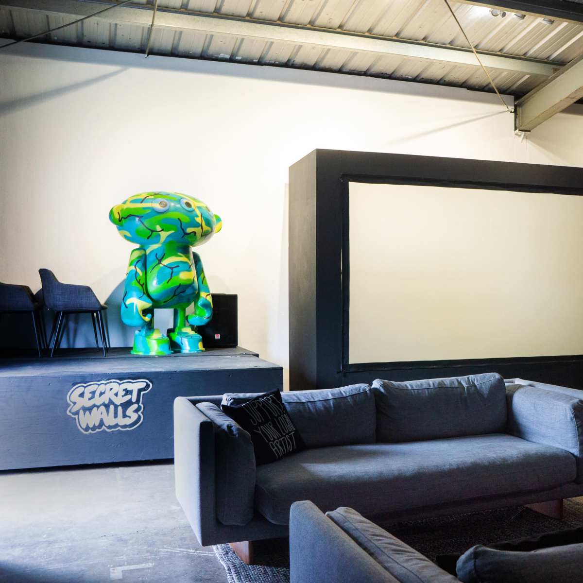 A spacious room with two large, colorful sculptures on pedestals and a blank wall framed by a sofa seating area.