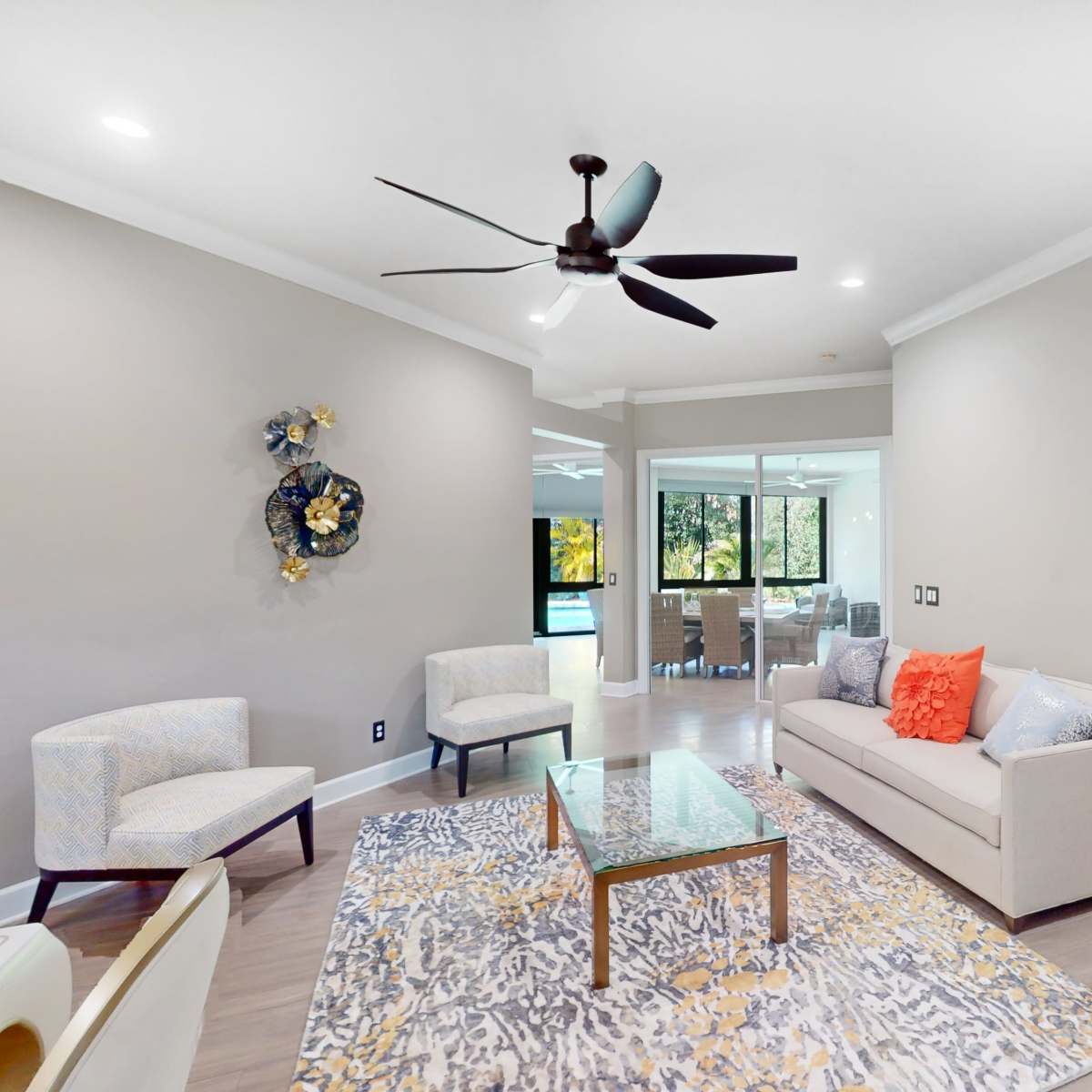 The living area features a sofa, two chairs, a glass coffee table on a patterned rug, and a ceiling fan.