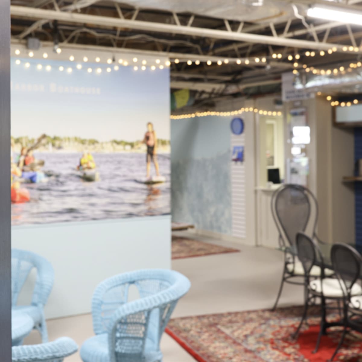 The interior of a beach-themed facility with a sign for "Little Harbor Bathhouse" and seating arranged around a cozy space decorated with string lights.