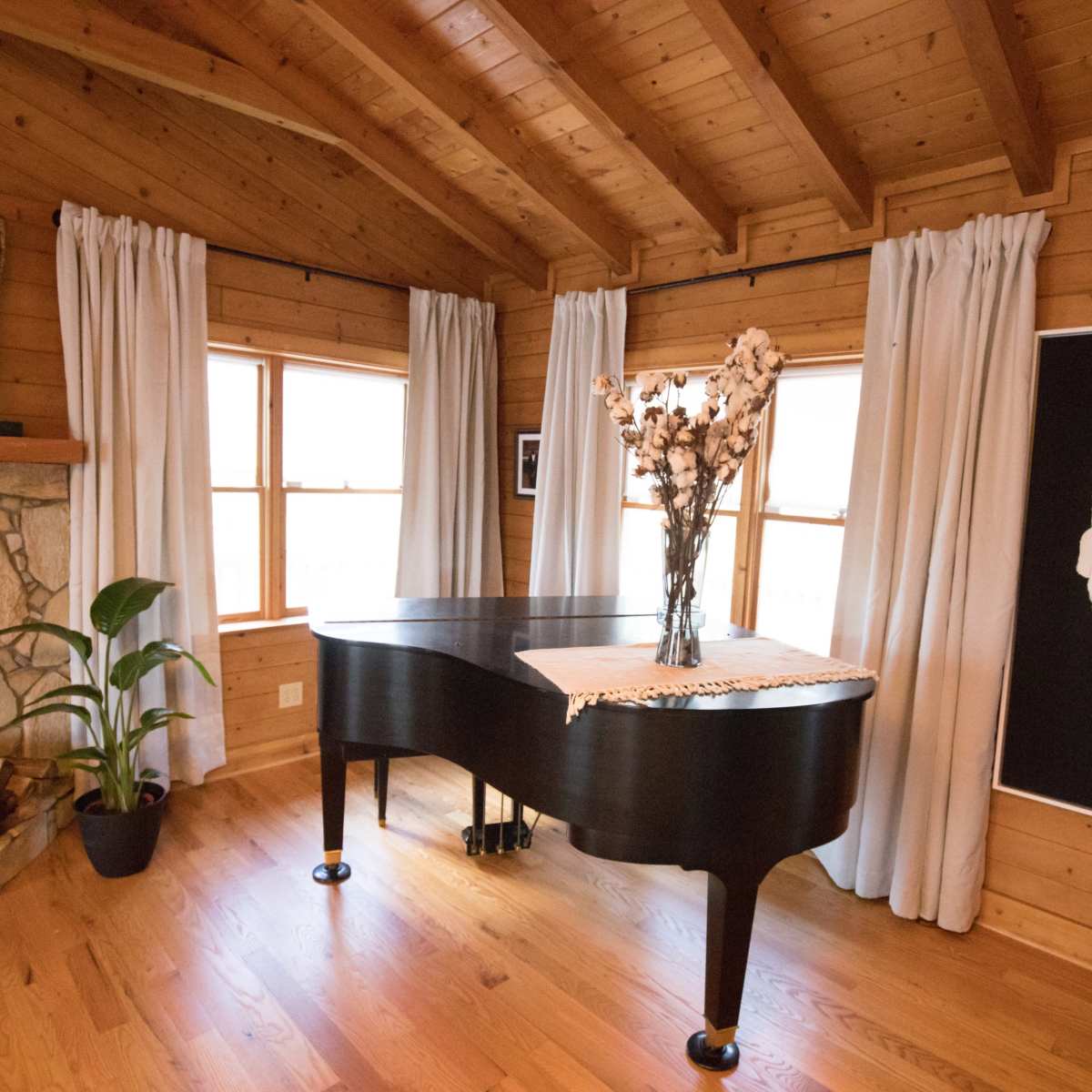 A grand piano is placed next to a stone fireplace in a room with wooden walls and large windows.