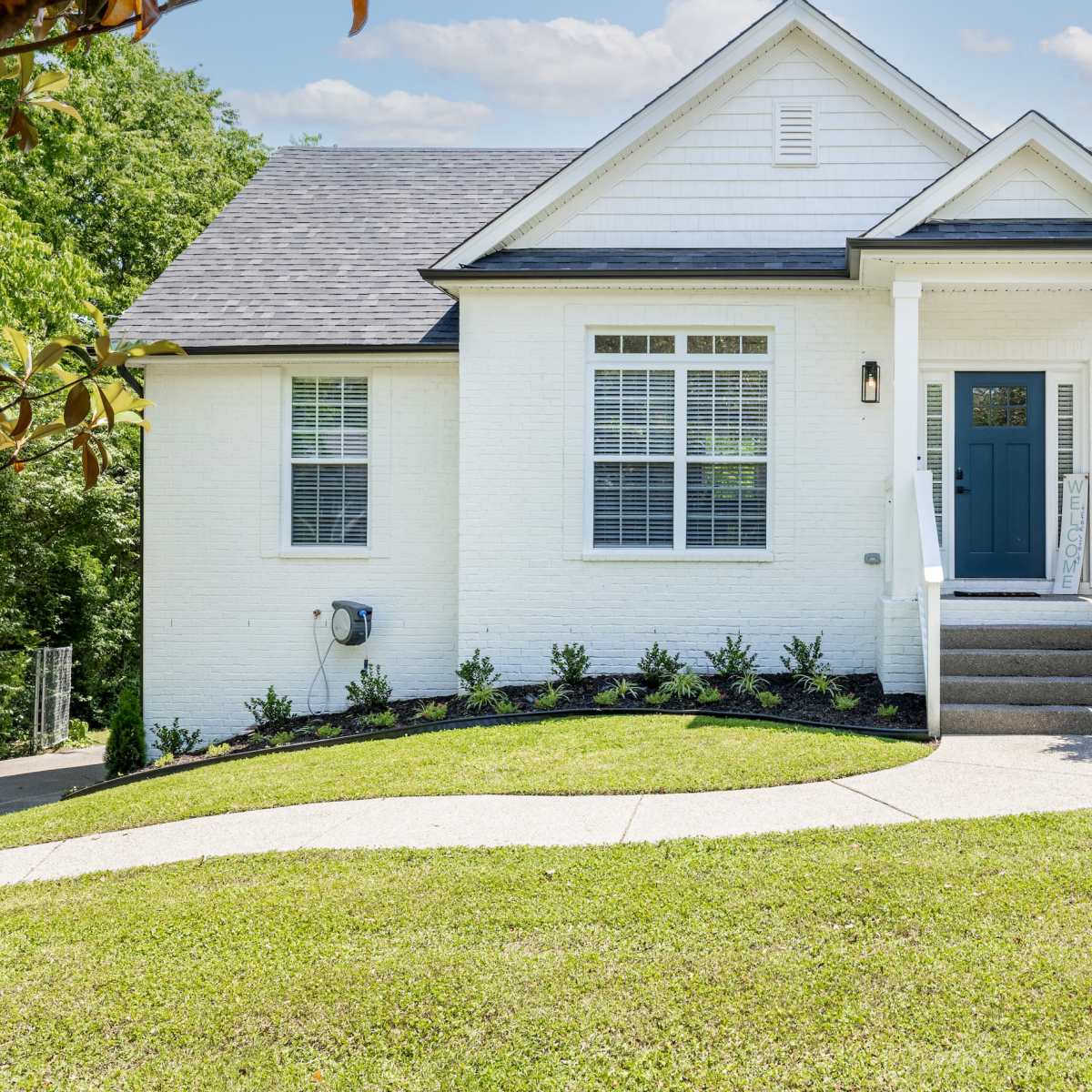 A single-story white house with a blue front door, surrounded by manicured landscaping and stone steps leading to the entrance.