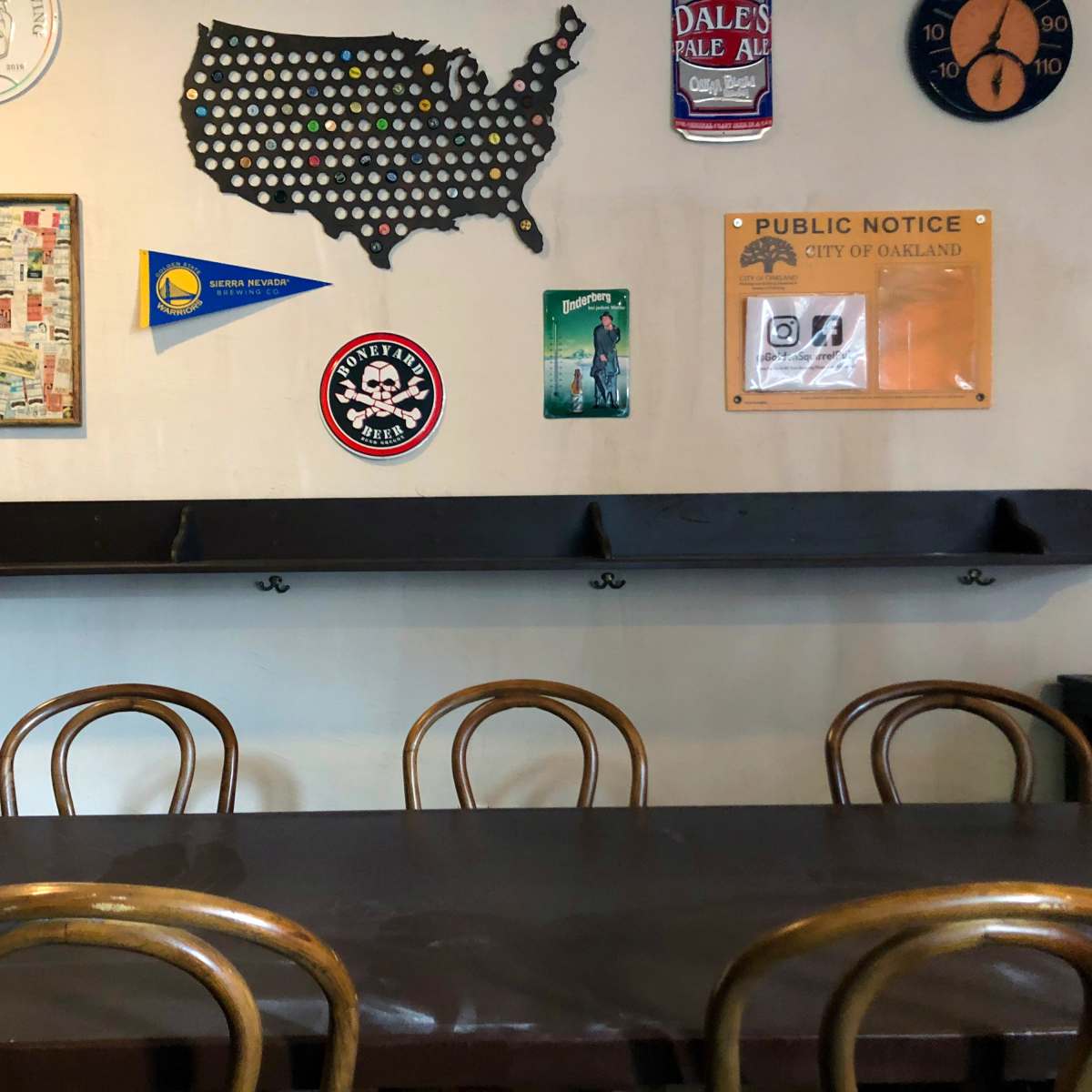 A wall adorned with various posters, signs, and a United States map, alongside a long wooden table with four chairs in front of it.