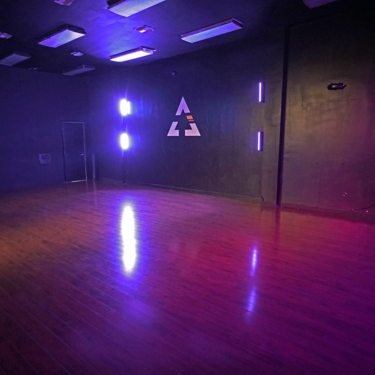 A dimly lit room with wooden flooring and purple neon lights illuminating one side of the wall.