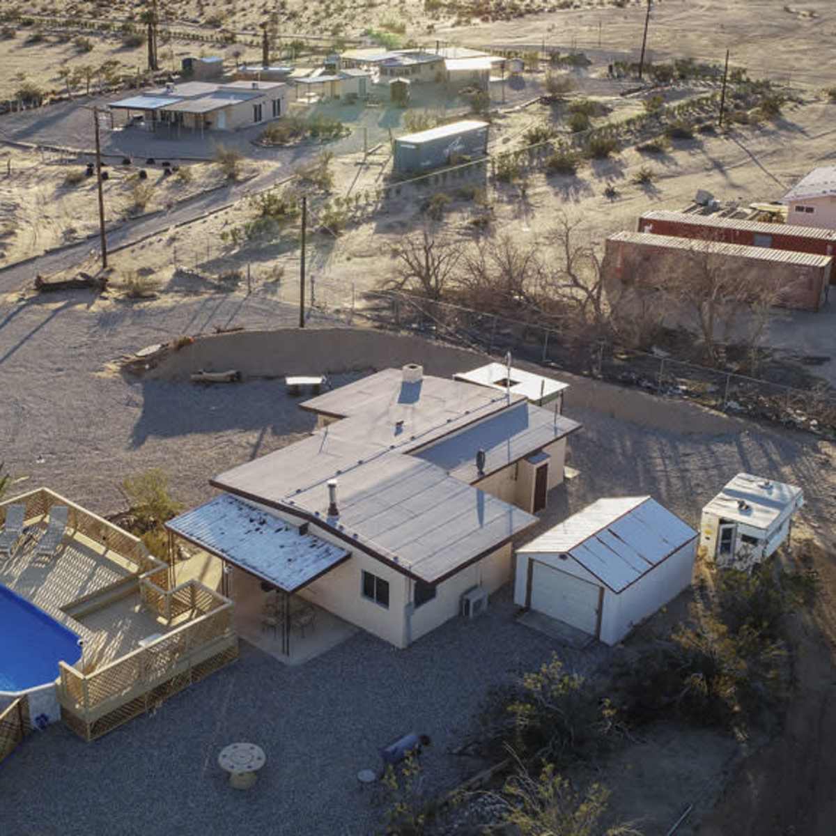 A cluster of buildings in a desert landscape, including a house with a pool, surrounded by gravel and sparse vegetation.
