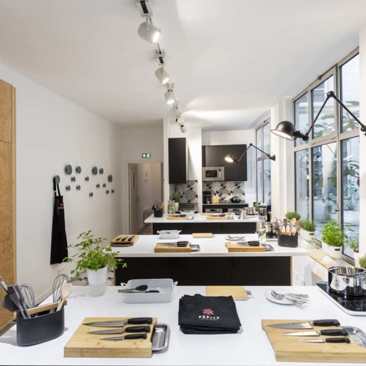 A modern kitchen with wooden cabinetry and multiple cooking stations equipped with utensils, knives, and potted plants.