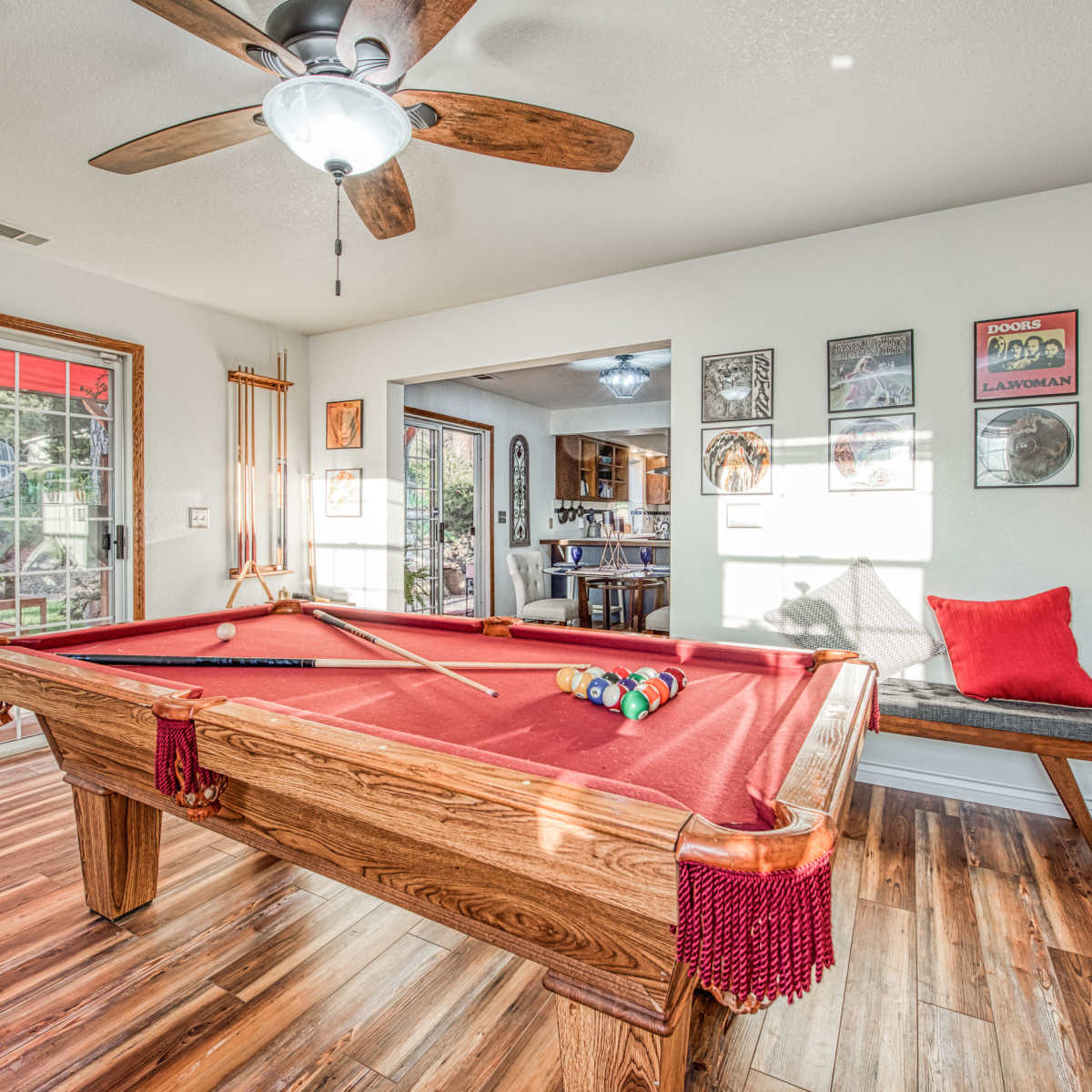 A well-lit game room featuring a red felt pool table, wooden ceiling fan, and walls adorned with framed artwork.