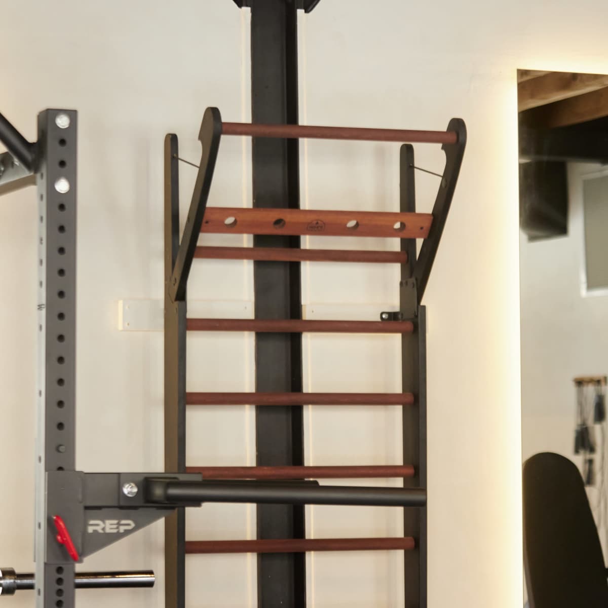 A wooden gym ladder mounted against a wall in a fitness space with exposed beams overhead.