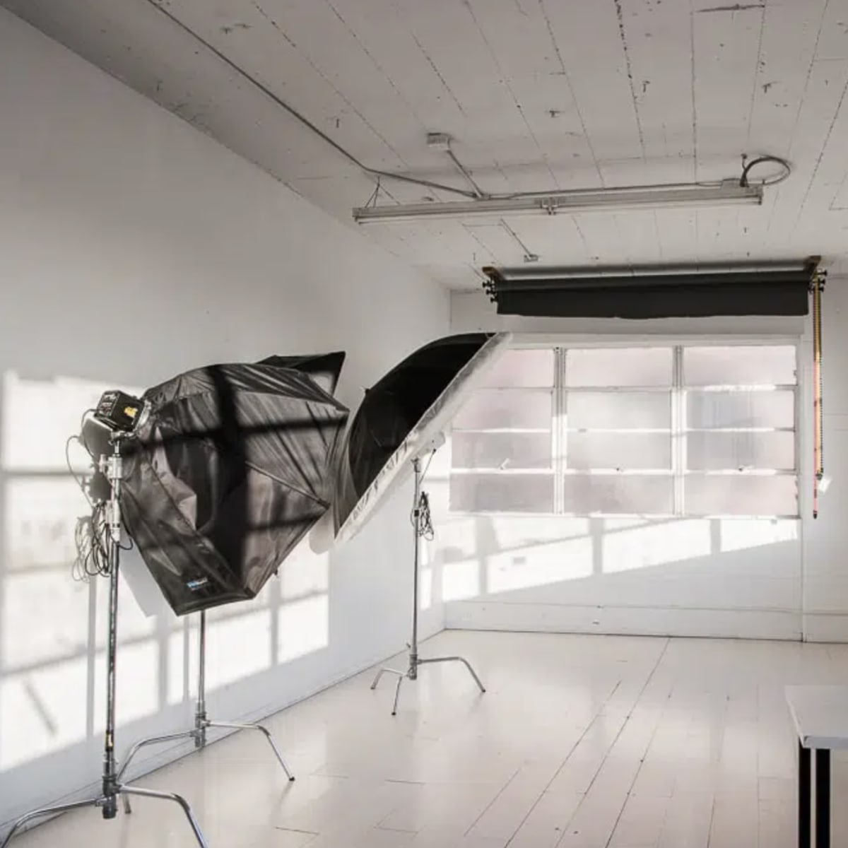 A well-lit photography studio with two softboxes positioned near a large window and a table in the corner.