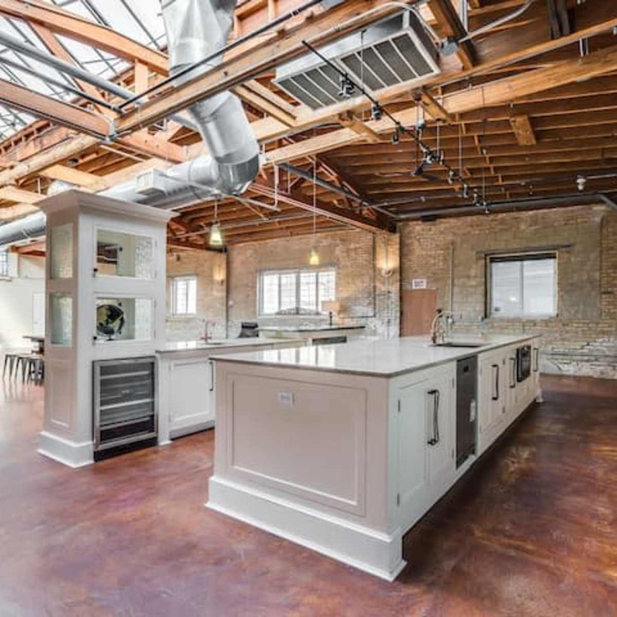 A spacious kitchen with a central island, high ceilings, exposed wooden beams, and large windows allowing natural light.