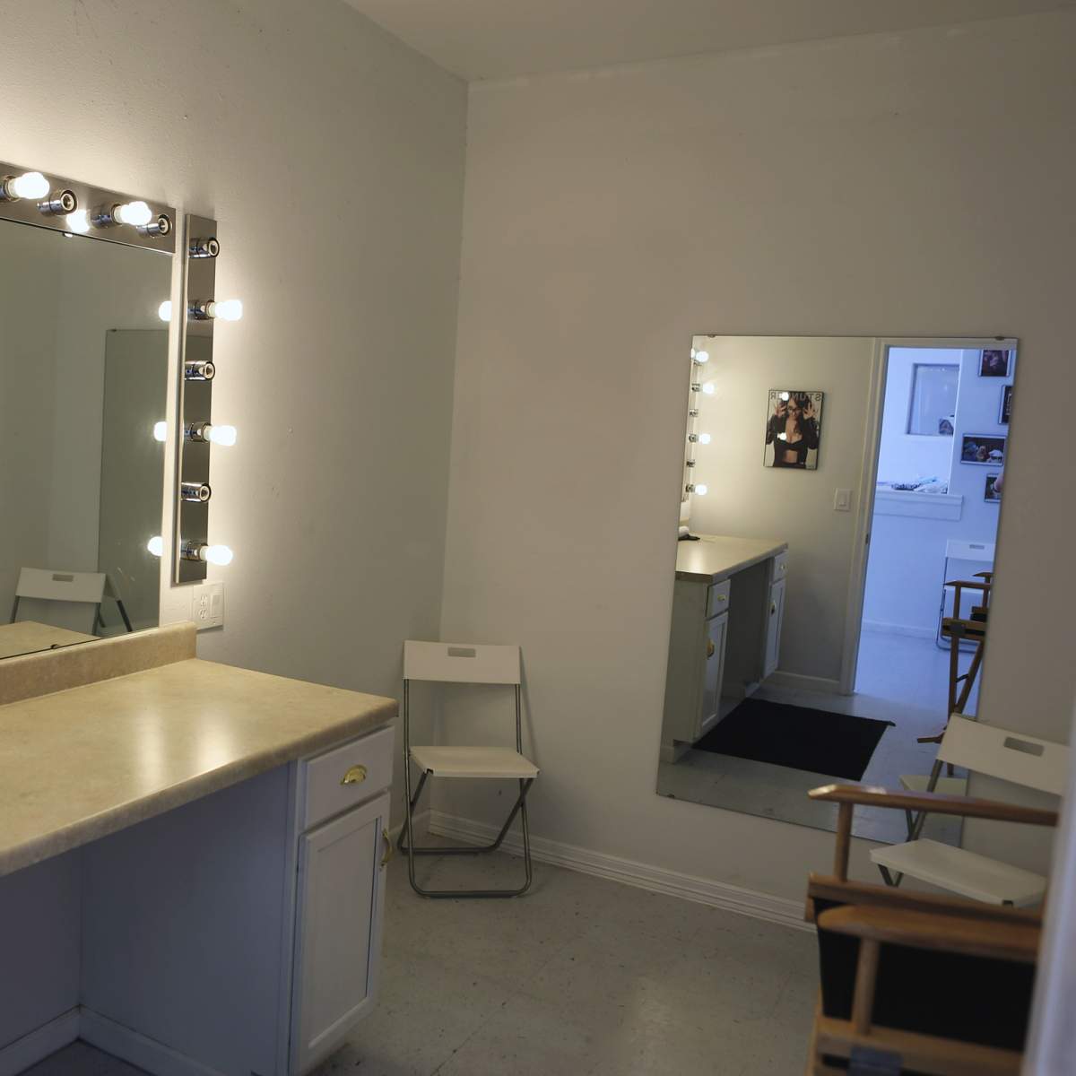 A well-lit dressing room with two mirrors, a countertop, and two folding chairs.