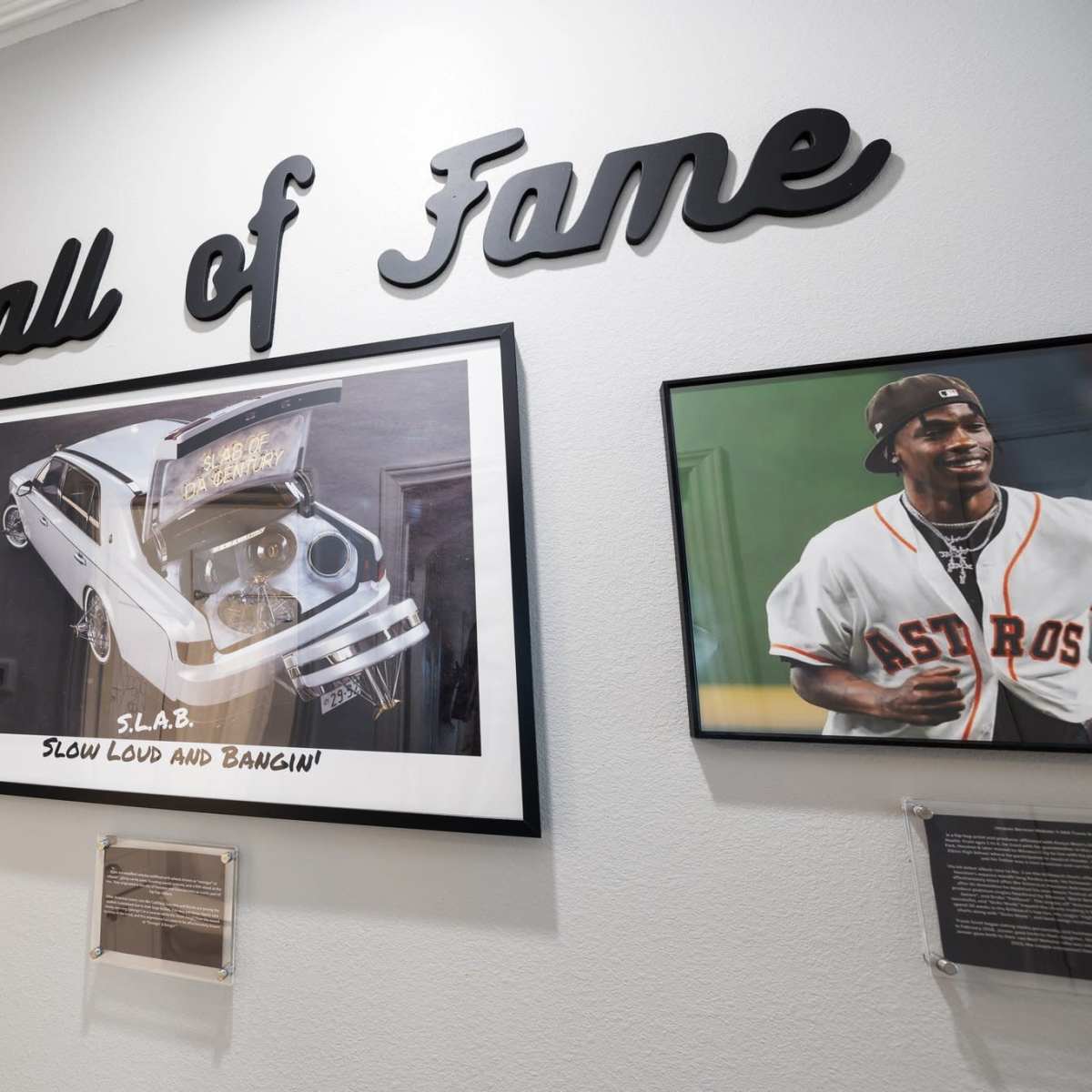 A wall labeled "Hall of Fame" with various framed photographs and artwork, including a central piece depicting a car and the text "S.L.A.B. SLOW LOUD AND BANGIN'."