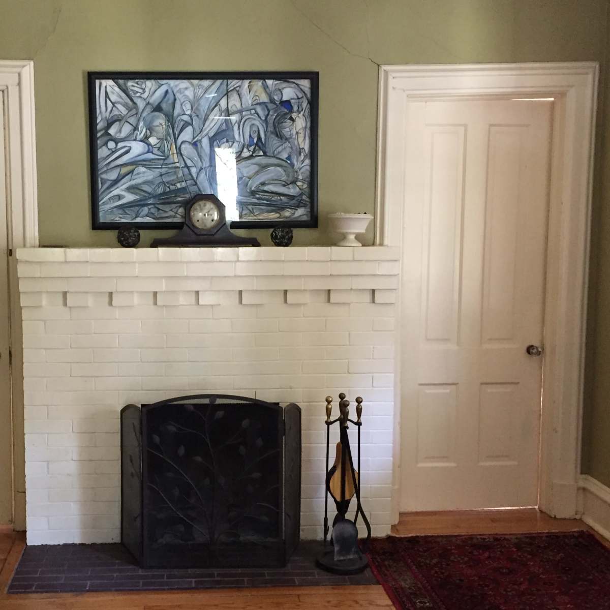 A white brick fireplace flanked by two closed white doors, with a clock and artwork above the mantel.