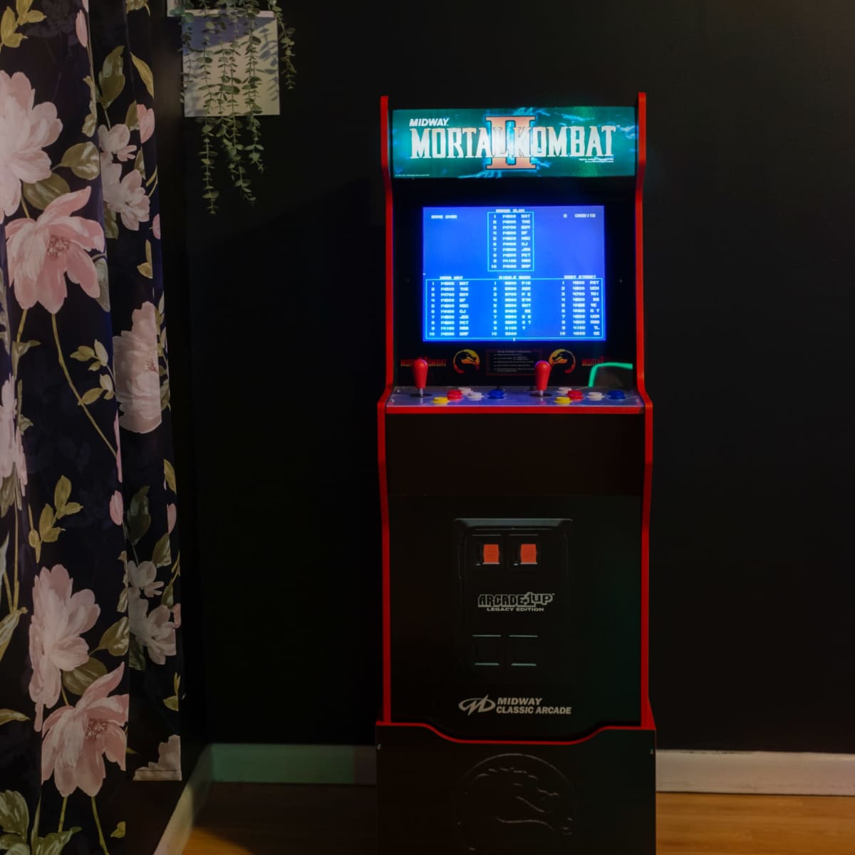 A retro Mortal Kombat arcade machine placed against a dark wall adorned with floral wallpaper.