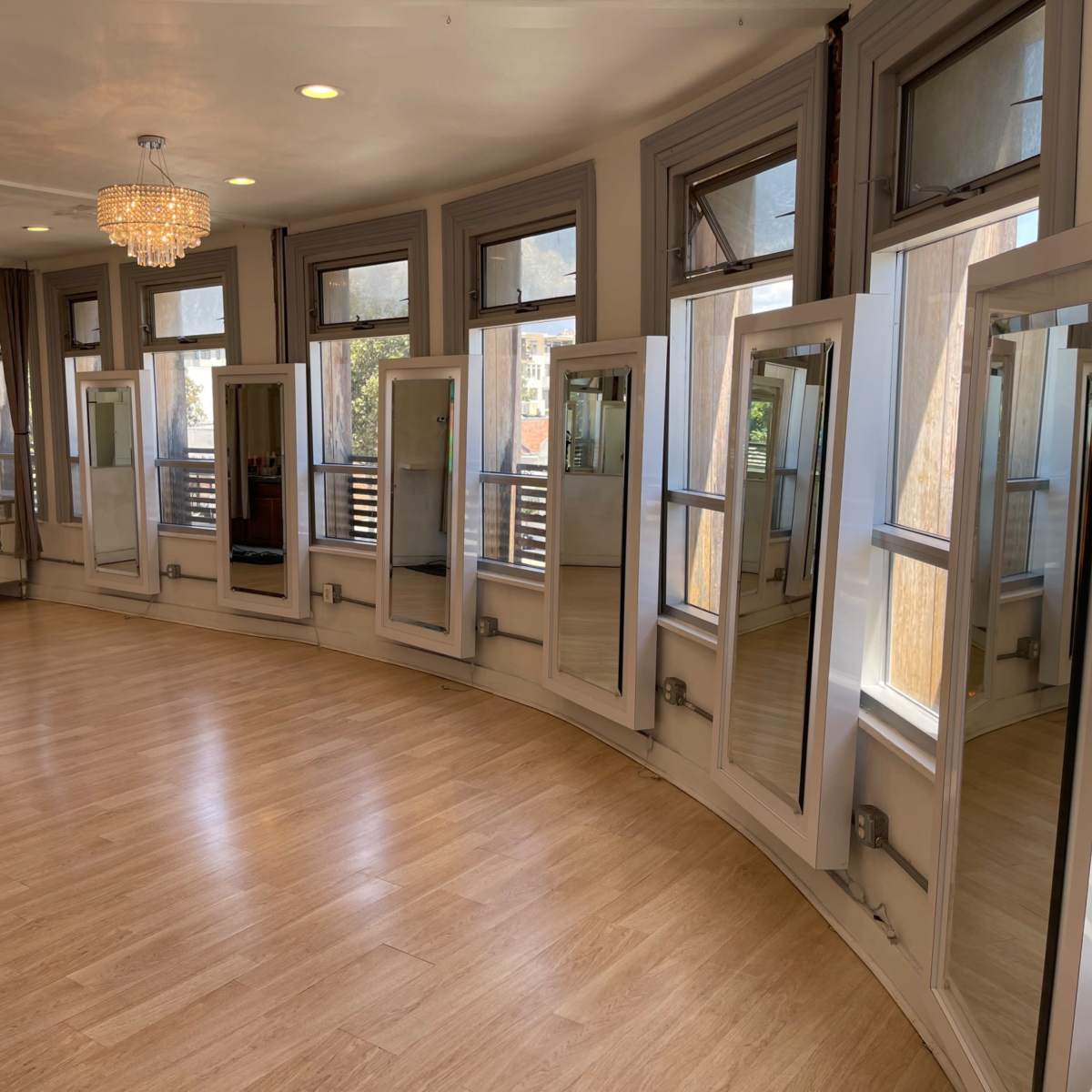 A spacious, curved interior room with multiple tall mirrors and large windows letting in natural light.
