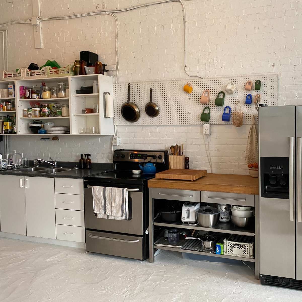 A kitchen area featuring a stainless steel refrigerator, a black stove, a wooden countertop, and various kitchen utensils hanging on a pegboard.