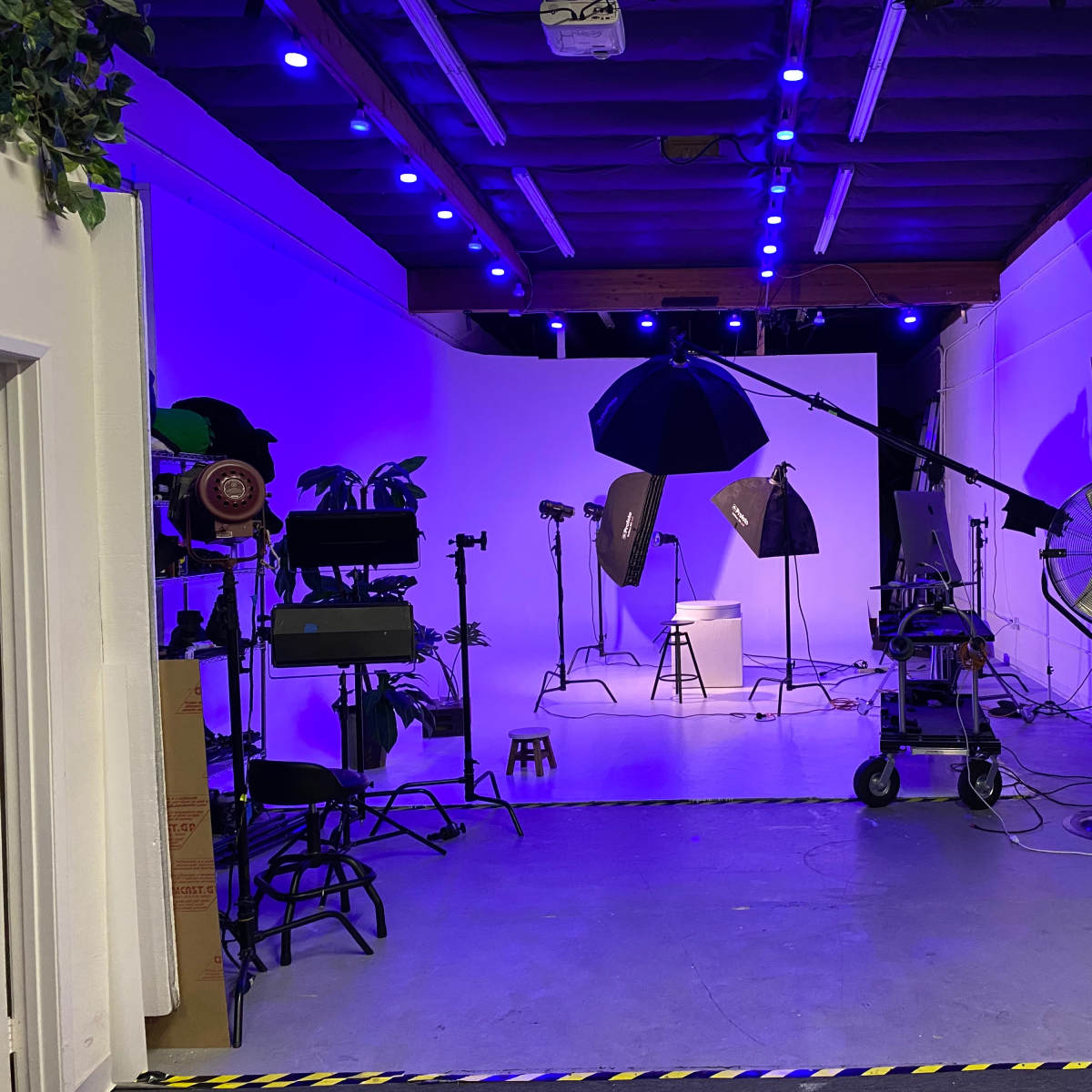 A photography studio is set up with lighting equipment, backdrops, and various props in a room with purple lighting.