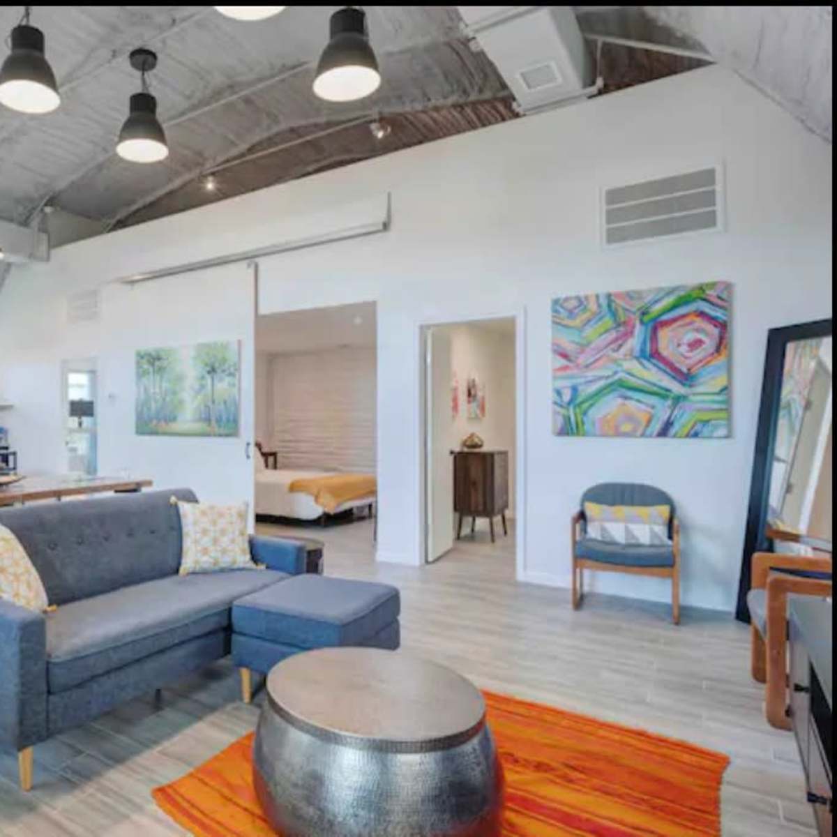 A modern, open-concept living space featuring a kitchen, dining area, and lounge with a blue sofa and colorful artwork on the walls.