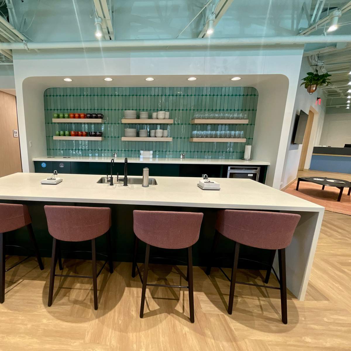 A modern kitchen area with a large island, four bar stools, and a wall featuring neatly arranged dishware and colorful containers.