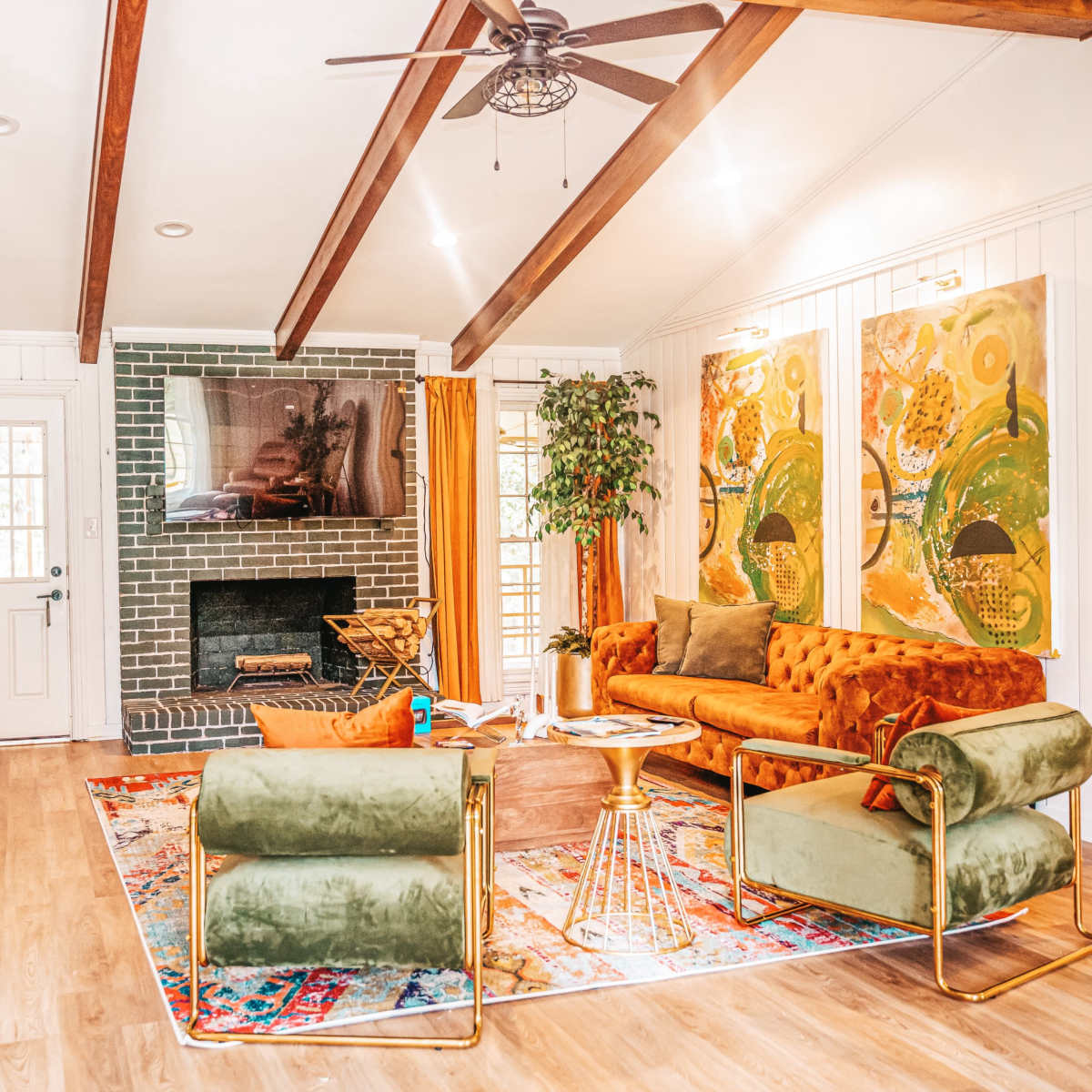 The room features a living area with a green brick fireplace, orange and green upholstered furniture, a large area rug, and two colorful wall art pieces.