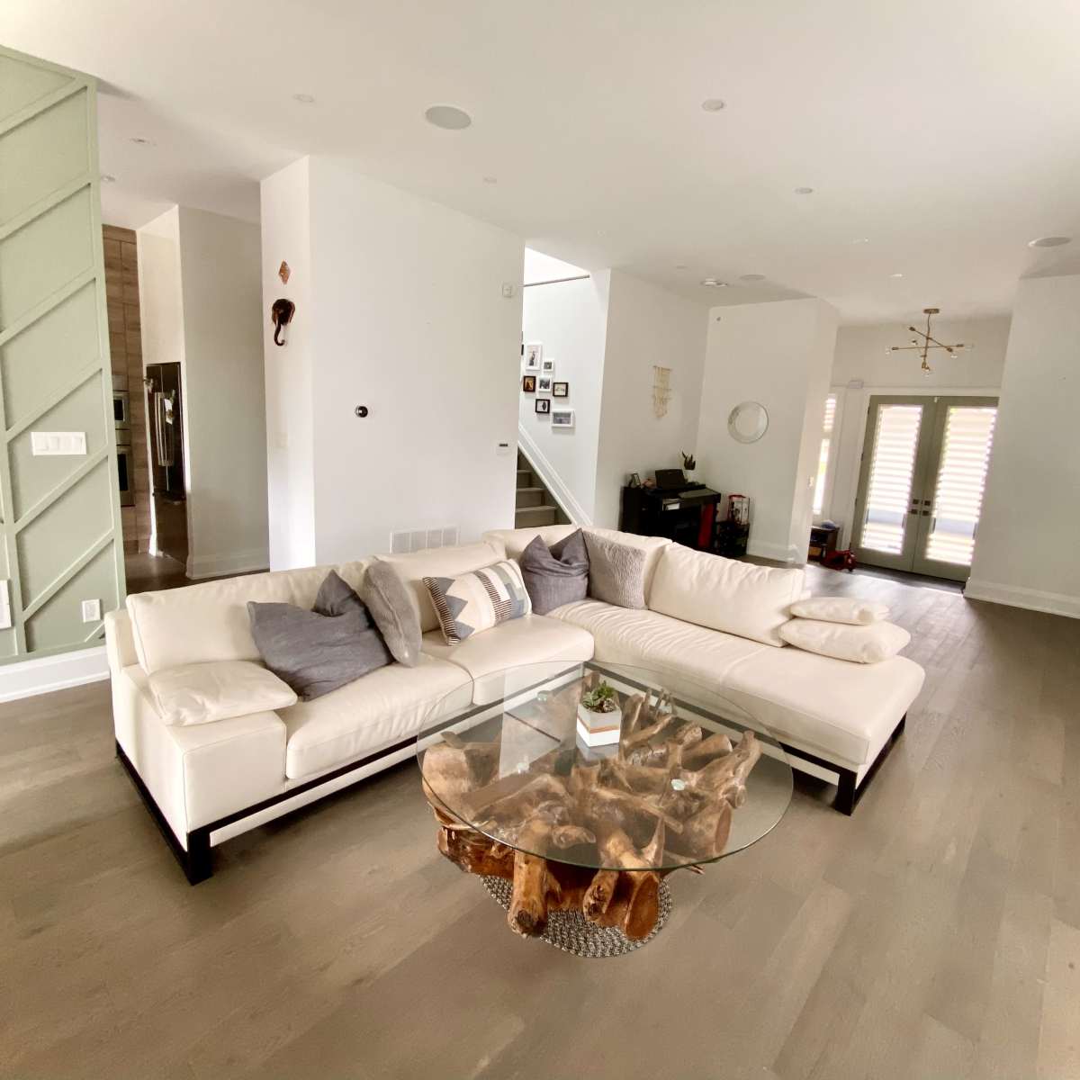 A modern living room featuring a large white sectional sofa, a glass coffee table made of wood, and neutral wall colors with minimal decorations.