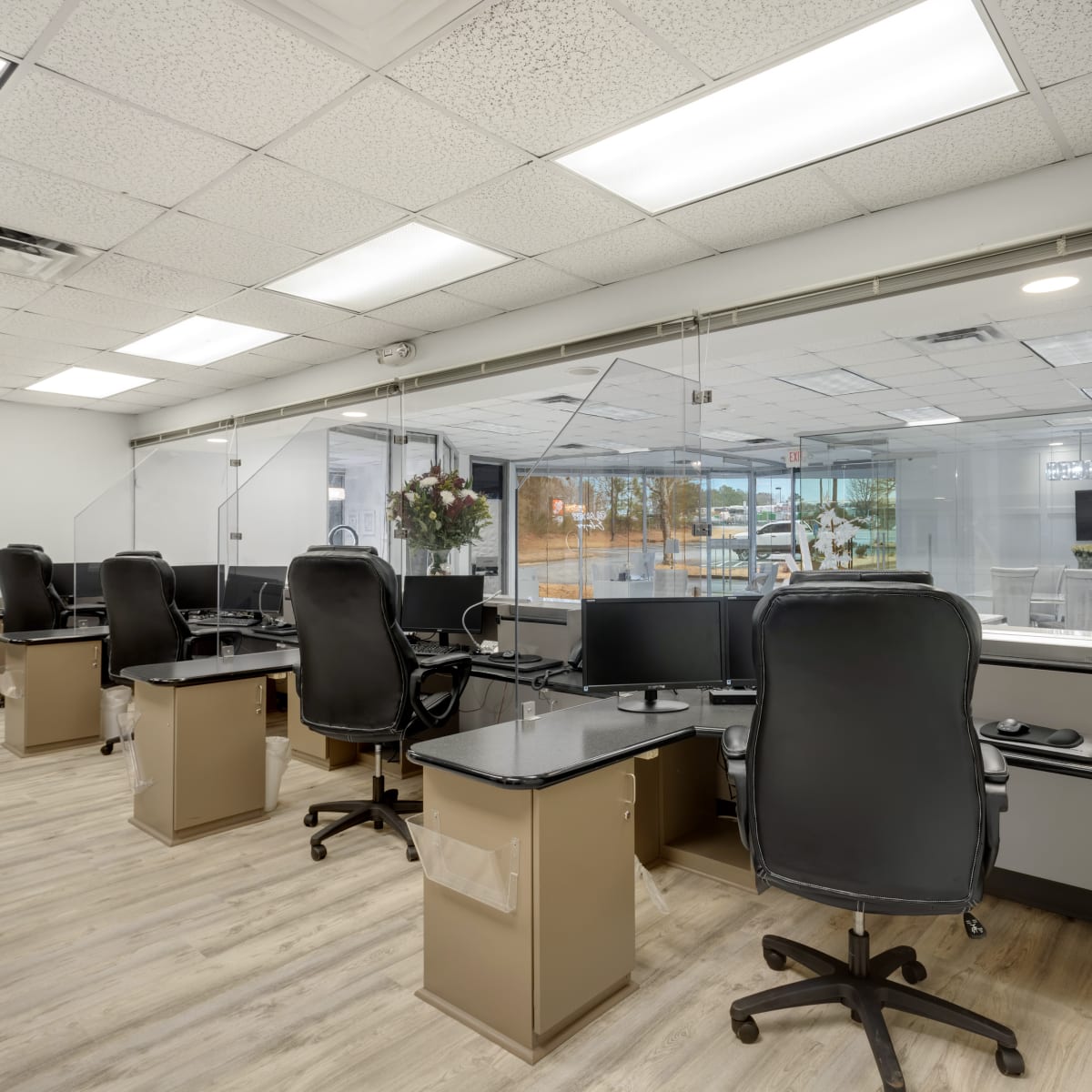 A modern office space with several workstations featuring desks, chairs, and partitioned acrylic dividers.