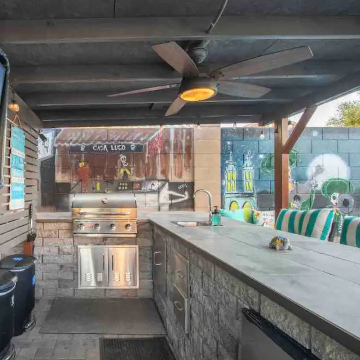 An outdoor kitchen area featuring a grill, counter space, and a mounted TV under a shaded structure.