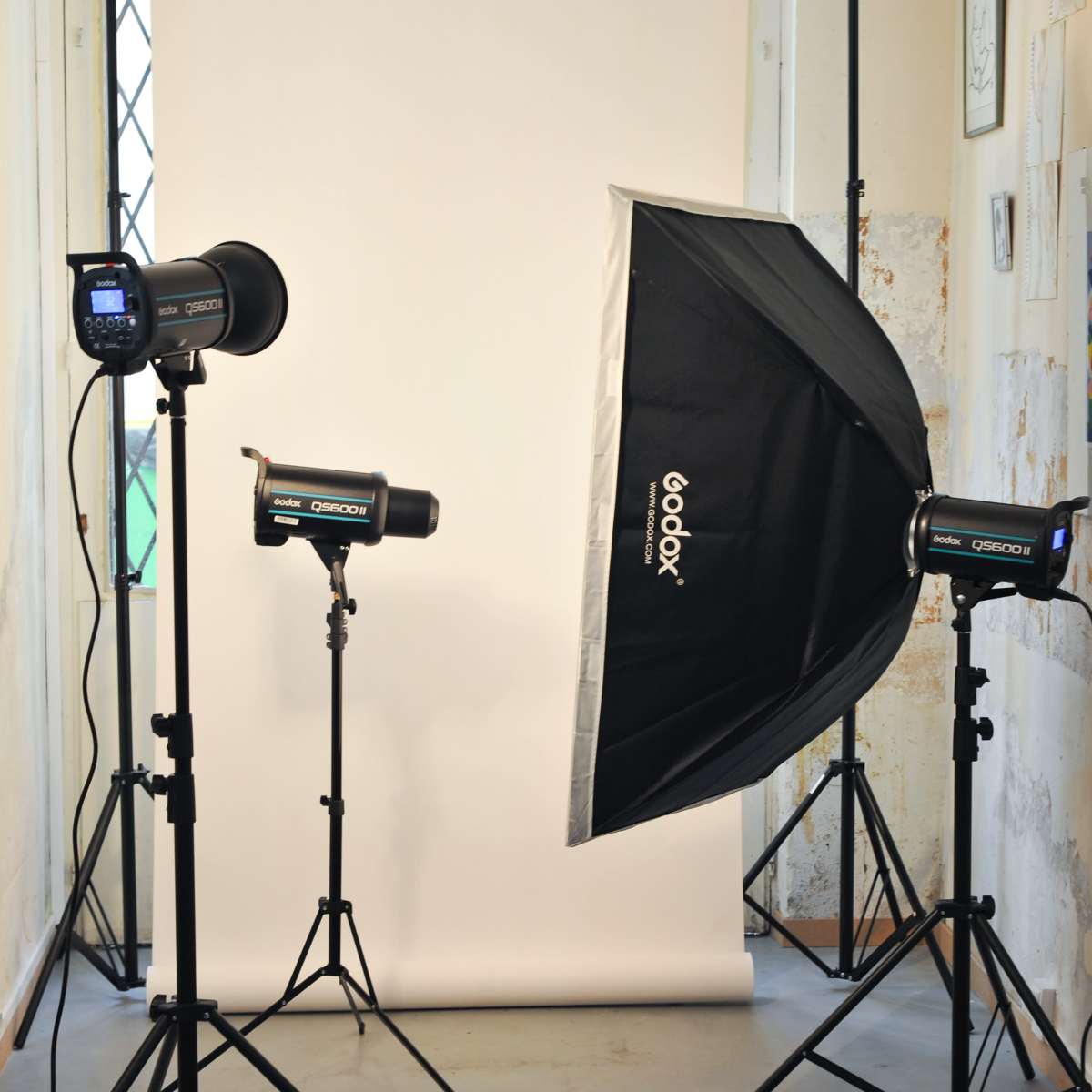 A photography setup with two Godox studio lights and a large softbox positioned on either side of a white backdrop in a room with exposed walls.