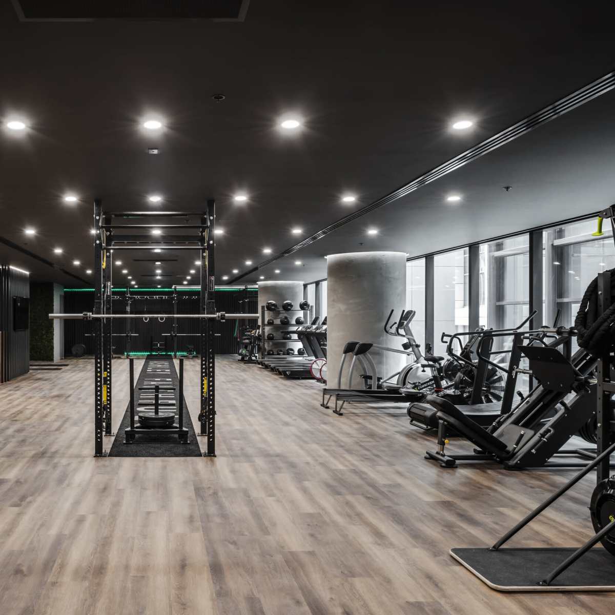 A modern gym interior featuring workout equipment, a lifting station, and large mirrors along the walls.