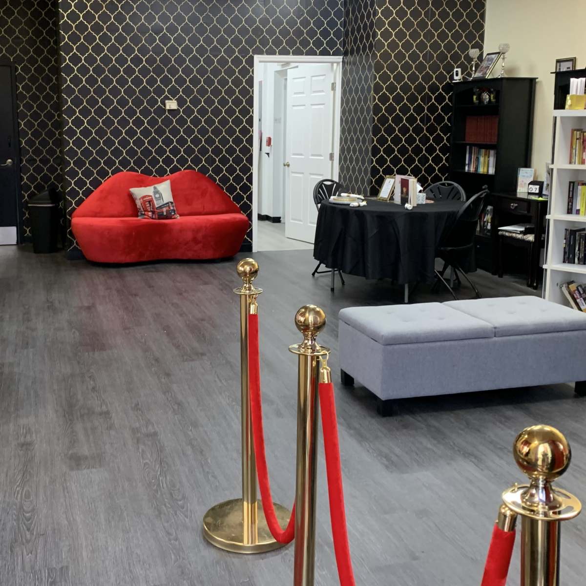 A modern interior space with a red couch, a gray ottoman, and a black table, separated by velvet ropes.