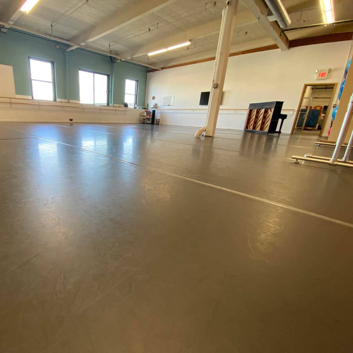 A spacious dance studio with a smooth gray floor, mirrored walls, and a piano in the corner.