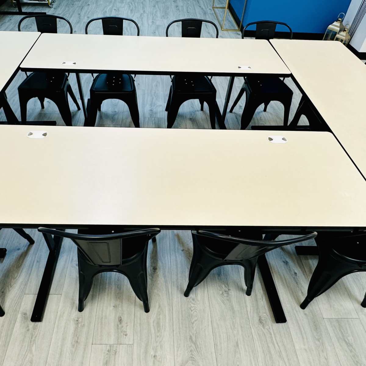 Several black chairs surround a square arrangement of pale tables in a light-colored room.