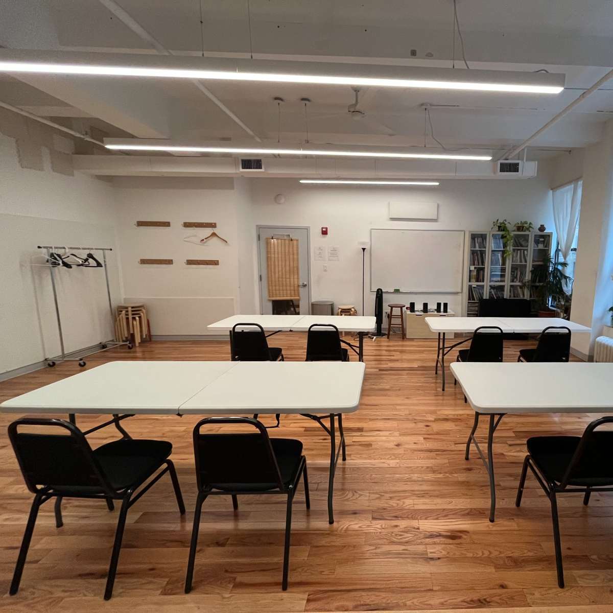 A spacious room with several tables and chairs arranged for a meeting, featuring large windows and wooden flooring.